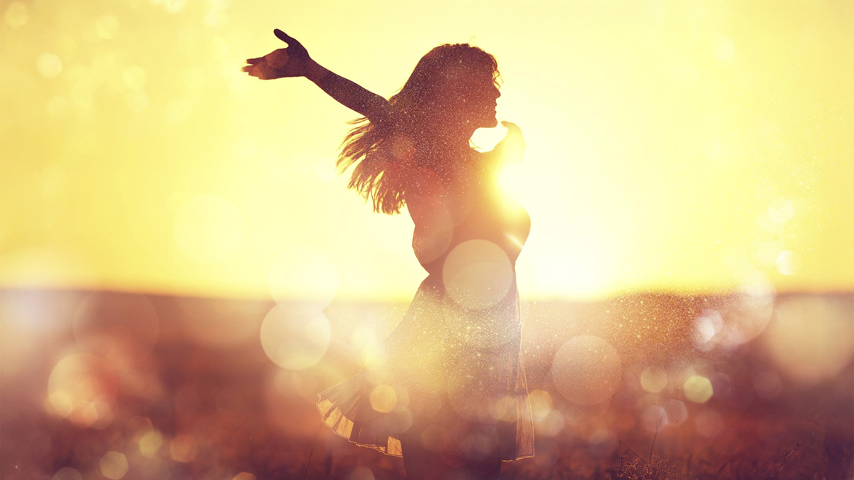 Mulher de braços abertos ao pôr do sol, simbolizando recomeço profissional, liberdade e propósito de vida.