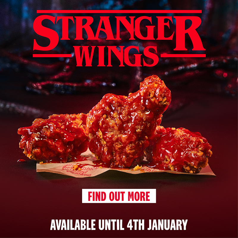 As Stranger Wings do KFC, frango empanado com molho vermelho inspirado no universo de Stranger Things, apresentadas sobre papel da marca em cenário sombrio que remete ao Mundo Invertido.
